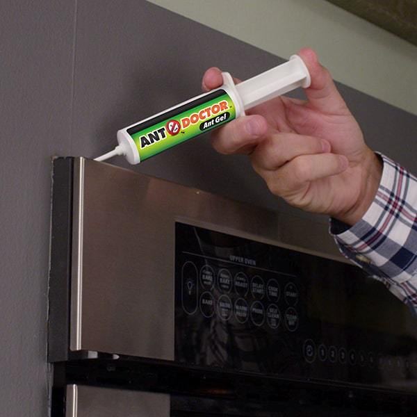 A close up of a man's hand holding an Ant Doctor and squeezing it onto the top corner of an oven